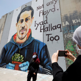 Una mujer palestina toma una fotografía a una amiga frente a una pintada en el muro con Israel que representa a Iyad al-Halaq, un palestino autista y desarmado que fue asesinado a tiros por la policía israelí, en Belén, en la Cisjordania ocupada. REUT