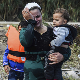 Una mujer afgana con un niño en brazos se emociona tras lograr alcanzar la costa a bordo de una lancha neumática en la isla de Lesbos (Grecia). EFE/Filip Singer