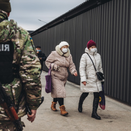 Dos mujeres caminan delante de un policía en el control fronterizo de Stanitsa Luganska para cruzar del territorio ucraniano al territorio de la autoproclamada República de Lugansk, a 17 de febrero de 2022, en Stanitsa Luganska, Oblas de Lugansk (Ucrani