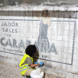 Operaria limpia los azulejos del mural publicitario datado en los años 20 y descubierto en las obras de la estación de metro Sevilla, en Madrid. / Consejería de Cultura