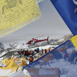 Banderas de oración enmarcan un helicóptero de rescate que transporta a los heridos del campamento base del Everest este domingo.- AFP PHOTO / ROBERTO SCHMIDT