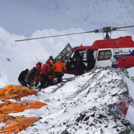 Una persona herida es subida a un helicóptero de rescate en el campamento base del Everest mientras los cadáveres de montañeros esperan ser trasladados, envueltos en sacos naranja.- AFP PHOTO / ROBERTO SCHMIDT