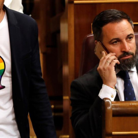 El presidente de Vox, Santiago Abascal, en uno de los escaños del Congreso de los Diputados, mientras pasa uno de los diputados del PSOE con 'gaysper' en su camiseta. - EFE
