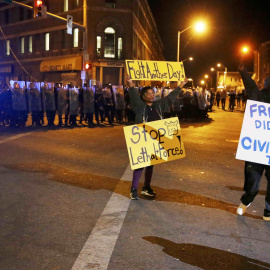 Protesters hold up signs in front of a line of police in Baltimore, Maryland. REUTERS/Jim Bourg
