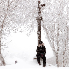 Un chico se sienta a los pies del Cruceiro de O Cebreiro en Lugo, que da entrada al Camino de Santiago en Galicia, cubierto por la nieve.
