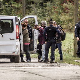 Gendarmes franceses llevan hasta unas furgonetas a los inmigrantes del campamento desalojado cerca del puerto de Dunkerque, en Francia.- AFP