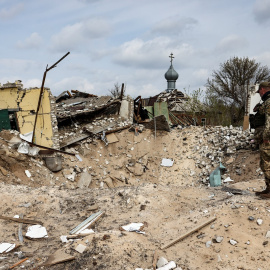 16/04/2022 Un militar ucraniano mira jacia un cráter y una casa destruida en la localidad de Yatskivka, en el este del país