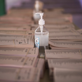 Un bote de gel hidroalcohólico corona una mesa llena de papeletas electorales en el Colegio Público Asturias en el distrito Puente de Vallecas, a 4 de mayo de 2021, en Madrid