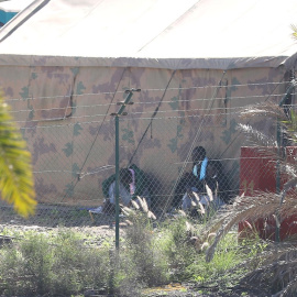Dos hombres se protegen del sol en la sombra de una tienda del centro para migrantes de Barranco Seco, en Gran Canaria.