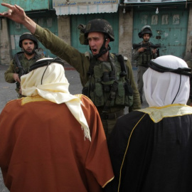 Un soldado israelí da órdenes a dos hombres palestinos durante una manifestación en Hebrón. - AFP
