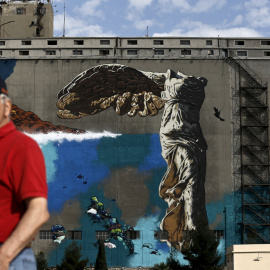 Un hombre pasa por delante de una pintada que reproduce la estatuta de la Vcotira de Samotracia, cerca del puerto del Pireo, en Atenas. REUTERS/Alkis Konstantinidis