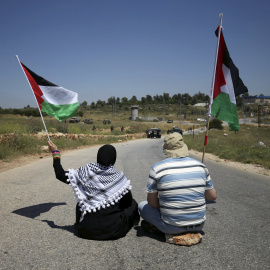 Protestantes palestinos sostienen banderas palestinas mientras militares israelíes toman posiciones durante una protesta contra los asentamientos ilegales en Cisjordania, al lado de Ramala./ REUTERS/Mohamad Torokman