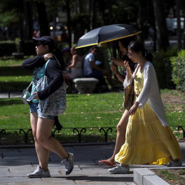Varios turistas se protegen del sol durante la ola de calor en el madrileño parque de El Retiro. / EFE