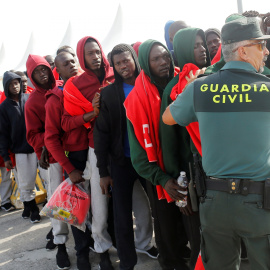 Migrantes parados por un guardia civil antes de ser distribuidos en autobuses - REUTERS