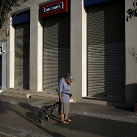 Una mujer con un carrito de la compra frente a una sucursal de Eurobank cerrada en Atenas, en una imagen de archivo. REUTERS / ALKIS KONSTANTINIDIS