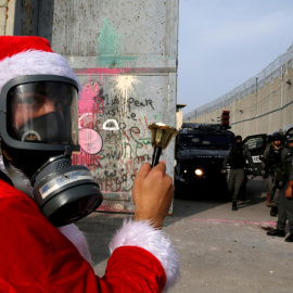 Un manifestante palestino vestido de Papá Noel protesta ante tropas israelíes en el muro que rodea la ciudad de Belén, ayer sábado 23 de diciembre. REUTERS/Ammar Awad