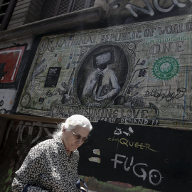 Una mujer pasa por delante de una pintada en Atenas que caricaturiza un billete de dólar. REUTERS/Alkis Konstantinidis