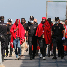 Efectivos de la Policía y miembros de Cruz Roja con varios de los 24 inmigrante, 22 hombres y dos mujeres, de origen subsahariano que han llegado al puerto de Almería.  EFE / Carlos Barba