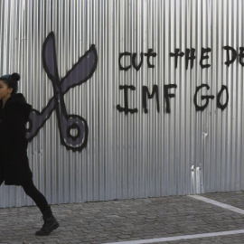 Una mujer pasea por el centro de Atenas junto a una pintura en contra del FMI.- REUTERS