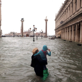 Una mujer sostiene a una niña mientras camina en una inundada plaza de San Marcos. Reuters / Manuel Silvestri