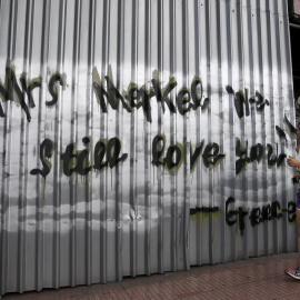 Una mujer corriendo por las calles de Atenas, pasa junto a una pintada que, en inglés, dice "Señora Merkel, todavía la queremos. Grecia". REUTERS/Alkis Konstantinidis