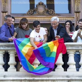 El alcalde de Valencia, Joan Ribó (centro), despliega desde el balcón del Ayuntamiento la bandera arco iris con motivo del Día Internacional del colectivo LGTB. /EFE