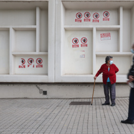 Dos personas mayores con mascarilla delante del Centro de Salud Pavones, donde hay carteles de protesta que rezan 'Urgencias Cerradas, tu salud vendida', a 21 de octubre de 2022, en Madrid.