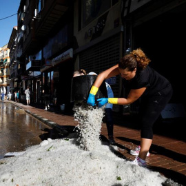 Dos ciudadanas vacían cubos de granizo en la calle después de la tormenta y la granizada que cayó este lunes en esta localidad causando importantes daños materiales.- EFE