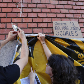 Dos jóvenes cuelgan una pancarta en la puerta de La Ingobernable.- EUROPA PRESS