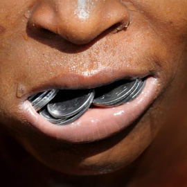 Un niño indio sostiene en el interior de la boca las monedas que ha recuperado del fondo del contaminado río Adi Ganga, en las proximidades del templo Kalighat en Calcuta, al este de la India. EFE/Piyal Adhikary