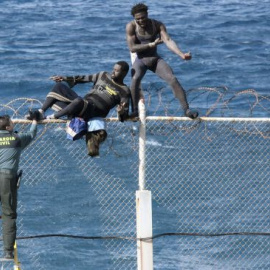 Dos inmigrantes intentan saltar la valla de Ceuta frente a un guardia civil. / Reduan (EFE)