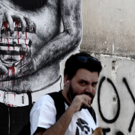 Un hombre pasa al lado de una pintada del símbolo del euro, en el centro de Atenas, hoy, el 14 de julio de 2015. AFP PHOTO / ARIS MESSINIS