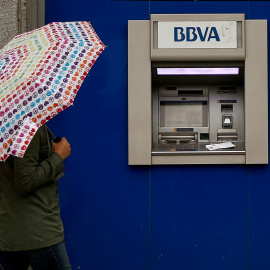Una mujer con paraguas junto a un cajero automático de una sucursal de BBVA en Madrid. REUTERS/Andrea Comas