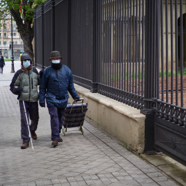 Una persona ciega camina junto a otra. 2020.