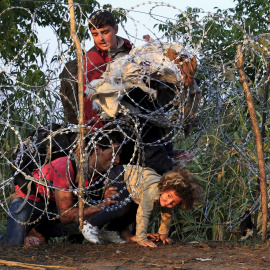Una niña junto a su familia, refugiados sirios, trata de cruzar la valla de cuchillas instalada por Hungría en su frontera con Serbia, cerca Röszke.- REUTERS / Bernadett Szabo