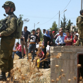 Palestinos esperan a poder cruzar un 'checkpoint' con soldados israelíes armados al sur de Hebrón. - AFP