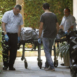 Miembros de los servicios funerarios trasladan el cadáver del hombre de 48 años localizado en un piso muy cerca de la entidad bancaria donde ha muerto a puñaladas su directora./ ANDREU DALMAU (EFE)