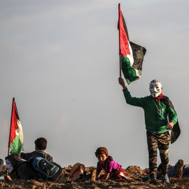 21/12/2018.- Un protestante palestino ondea una bandera nacional durante los enfrentamientos cerca de la frontera entre Israel y la Franja de Gaza, hoy, 21 de diciembre de 2018. Un menor palestino murió y doce resultaron heridos hoy por dis