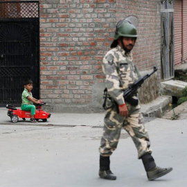 Un niño indio juega con su coche mientras un solado monta guardia durante el toque de queda en Srinagar después de las protestas por lamuerte un insurgente separatista hace 14 días/EFE