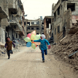 Niños sirios juegan con globos entre edificios dañados en el barrio de Jobar, a las afueras de la capital siria de Damasco. AMER ALMOHIBANY / AFP