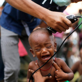 Un niño migran rohingya llora mientras un voluntario le corta el pelo en un centro temporal para refugiados en Indonesia.- BEAWIHARTA (REUTERS)