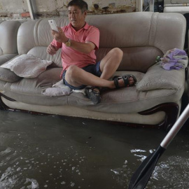 Fotografía que muestra a un hombre sentado en un sofá mientras toma fotos de las inundaciones, en Shenyang, provincia de Liaoning, al nordeste de China. EFE/Stringer