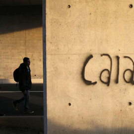 Varios inmigrantes caminan tras un muro en el que está escrito Calais, cerca de las instalaciones del eurotúnel que comunica Francia con Inglaterra. crisis. REUTERS/Pascal Rossignol