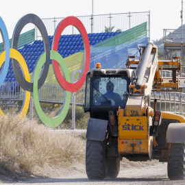 Un vehículo de construcción pasa cerca de unos anilllos olímpicos en una instalación en Barra de Tijuca. /EFE