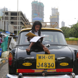 Una niña estudia sentada encima de un taxi al lado de su casa en Bombay./ REUTERS/Shailesh Andrade