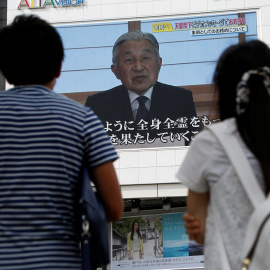 Un par de personas observan en una pantalla en la calle en Tokio el mensaje del emperador Akijito. REUTERS/Kim Kyung-Hoon