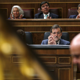 El presidente del Gobierno, Mariano Rajoy, observa al ministro de Economía, Luis de Guindos, durante su intervención en el pleno del Congreso.- REUTERS