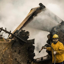 Un bombero refrescan los rescoldos tras incendiarse una casa en Fuchal, isla de Madeira (Portugal). Los tres fallecidos en los incendios que azotan Funchal, la capital del archipiélago luso de Madeira, son de la misma familia y hay un total