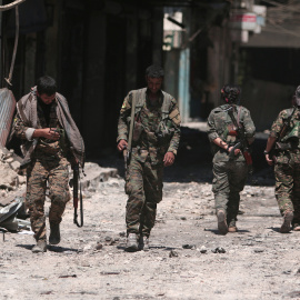Combatientes de las Fuerzas Democráticas de Siria (SDF) caminan sobre los escombros de tiendas y edificios dañados en la ciudad de Manbij, en Alepo, Siria. REUTERS / Rodi Said