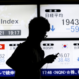 Un hombre pasa junto a un tablero electrónico que muestra el índice de precios de acciones de varios países asiáticos fuera de una casa de valores en Tokio. REUTERS